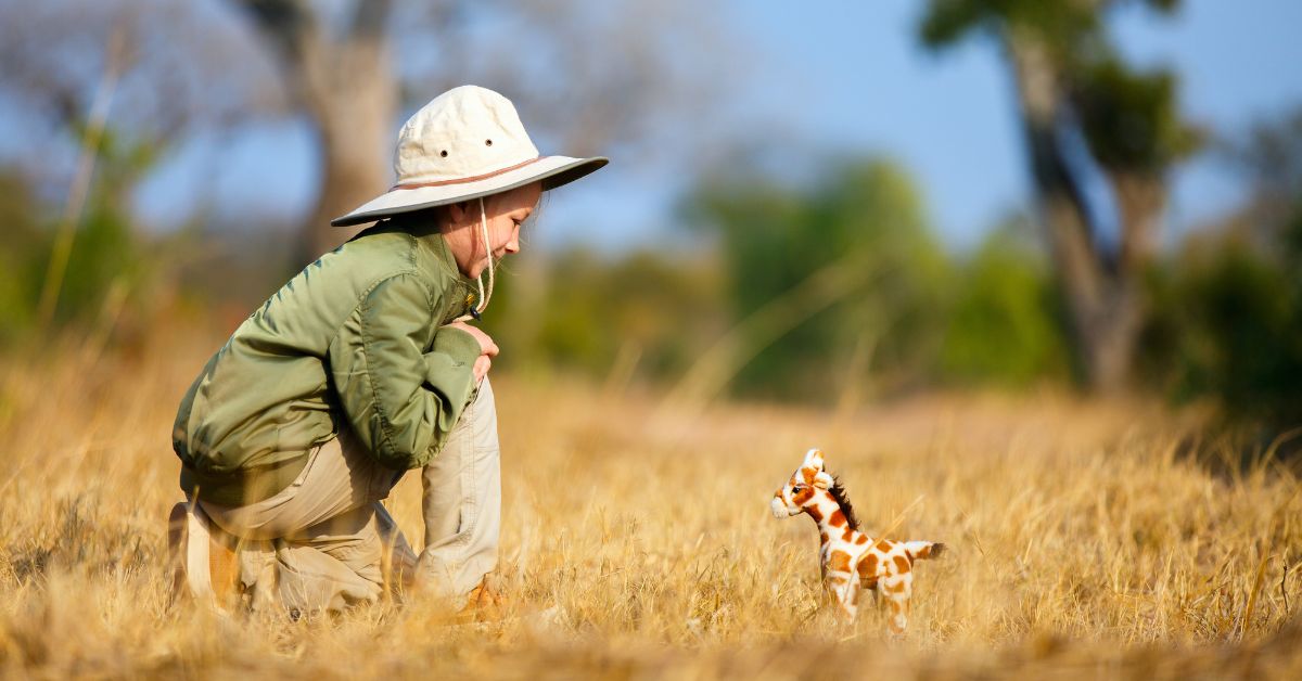 A young child wearing a safari hat crouched in the dry grass watching a small animal on a family safari.