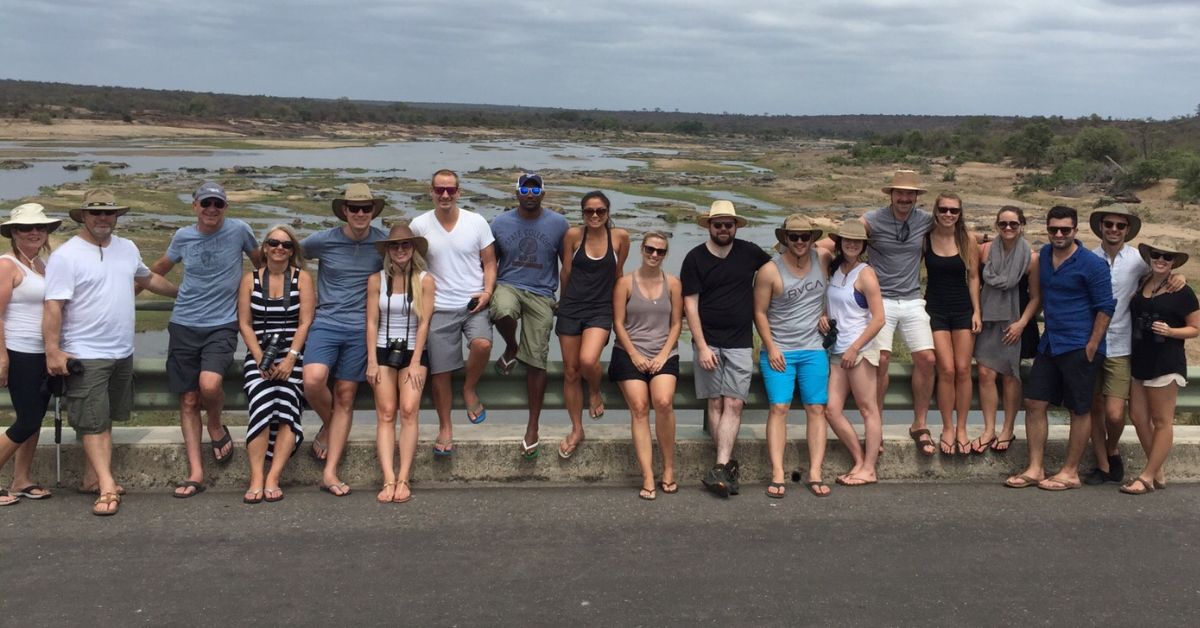 A smiling group of tourists standing together for a photo at a riverside scenic viewpoint during a Kruger National Park safari.