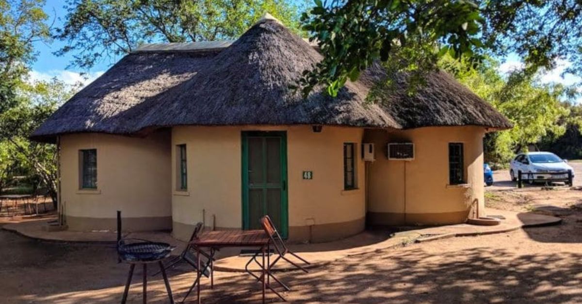 A circular thatched-roof bungalow with a private outdoor table, chairs, and a braai stand at Lower Sabie Rest Camp.