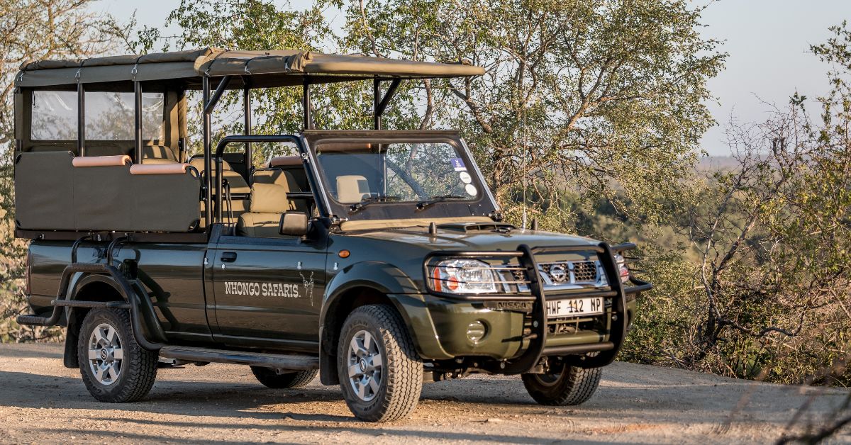 A green open-sided safari vehicle parked on a dirt road in the African bushveld on a kruger safari under a clear sky.