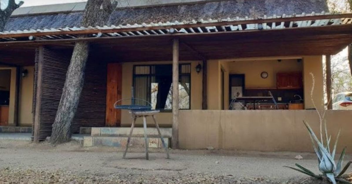 A beige thatched bungalow at Orpen Rest Camp with a private outdoor kitchen area and a braai stand in front of the veranda.