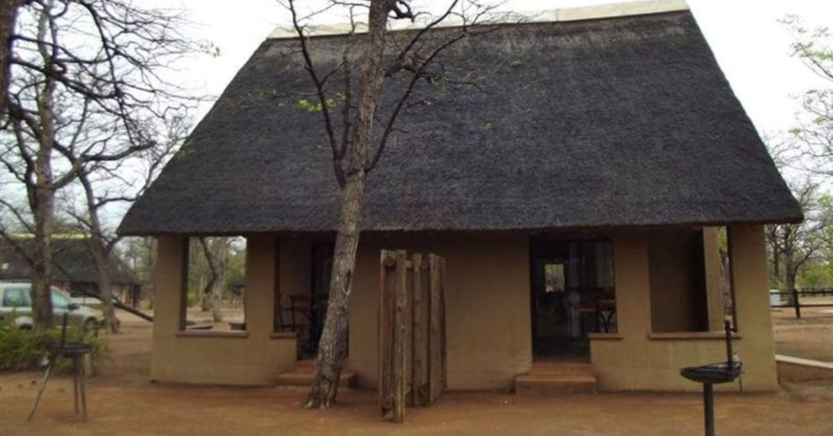 A traditional earth-toned bungalow with a steep thatched roof and a private porch at Shingwedzi Rest Camp in Kruger National Park.