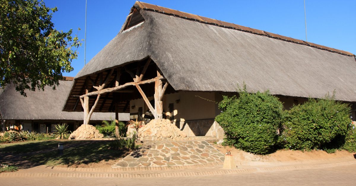 A scenic view of a large thatched-roof building at Skukuza Rest Camp under a clear blue sky, representing top-tier lodging in Kruger National Park.