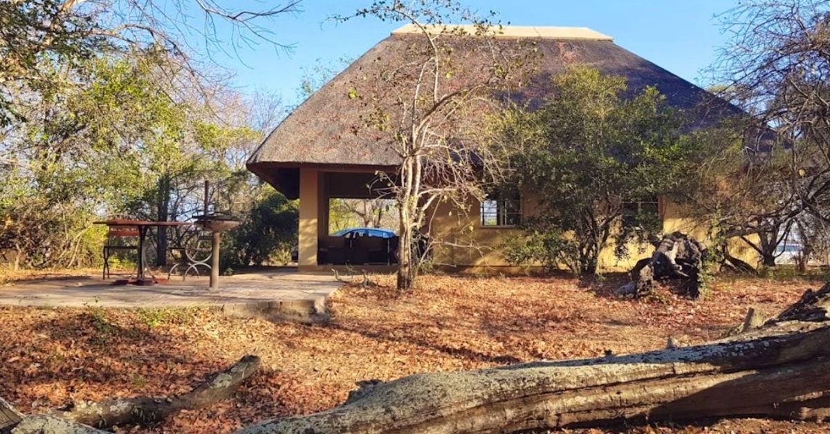 A beige thatched safari chalet with a covered porch and an outdoor dining table and braai area, surrounded by natural bush and dry leaves at Talamati Bushveld Camp.