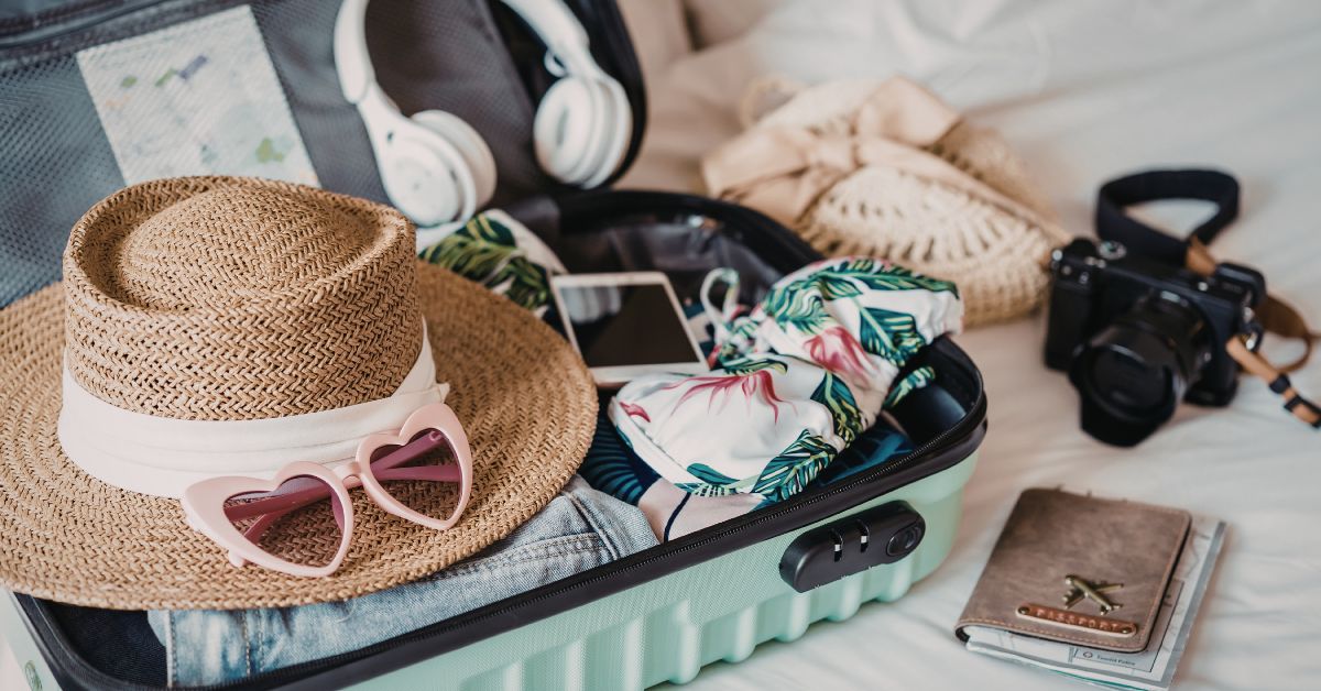 An open suitcase packed with a sun hat, sunglasses, clothing, camera, and travel essentials from a complete kruger safari packing guide.